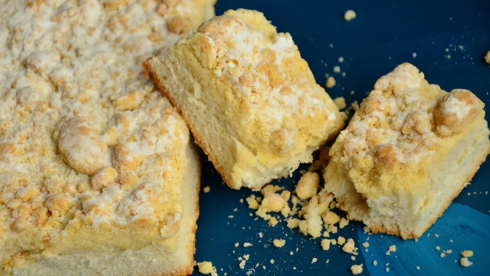 A freshly baked crumb cake with a golden, buttery crumb topping served on a white plate.