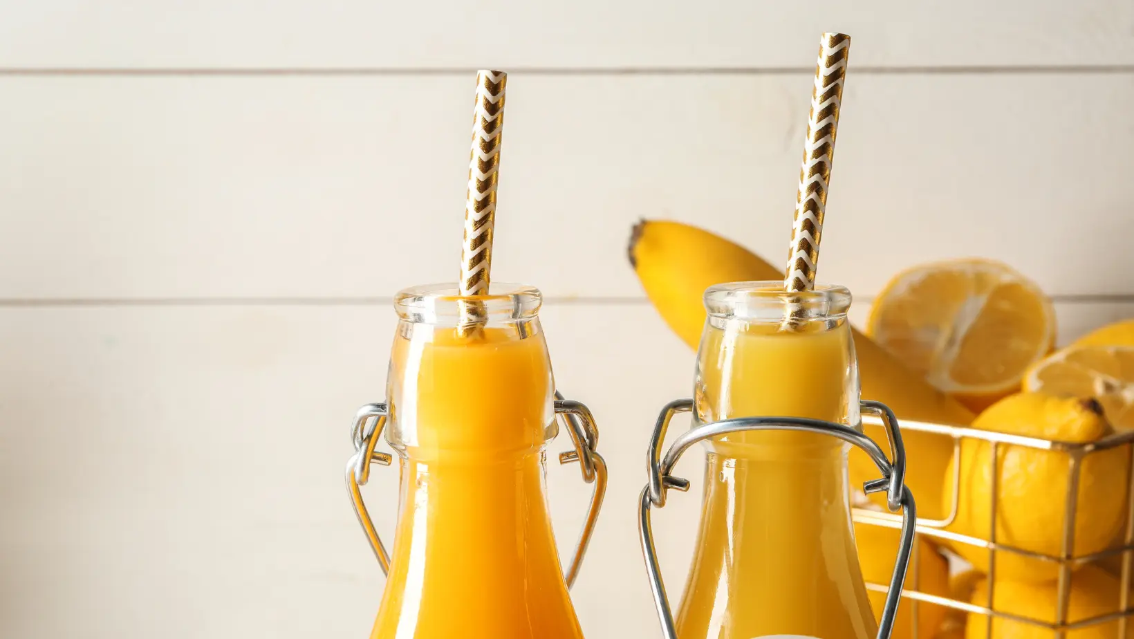 Bottled lemon juice next to fresh lemons on a wooden kitchen counter.