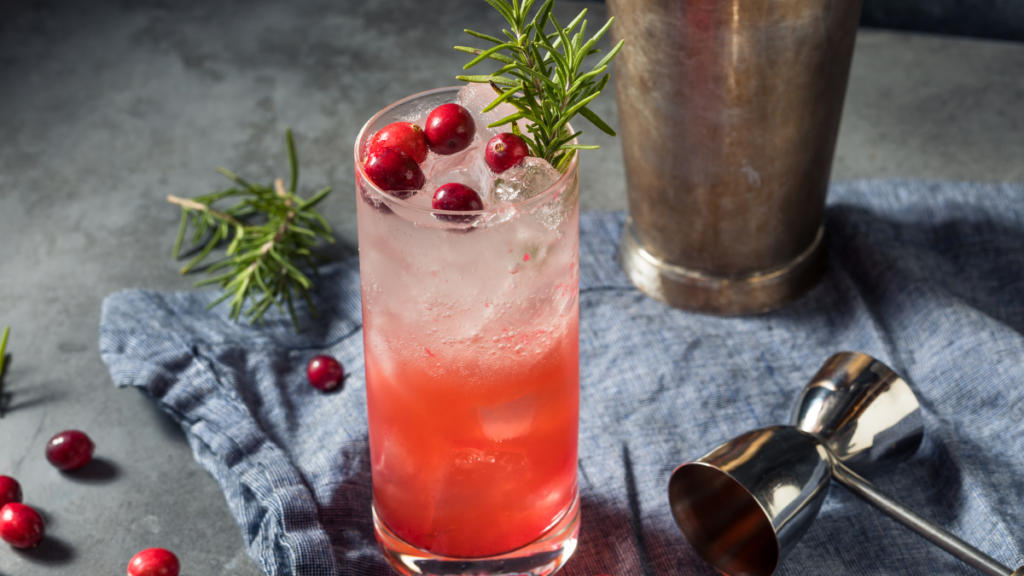 Glass of cranberry juice and champagne garnished with fresh cranberries and rosemary.