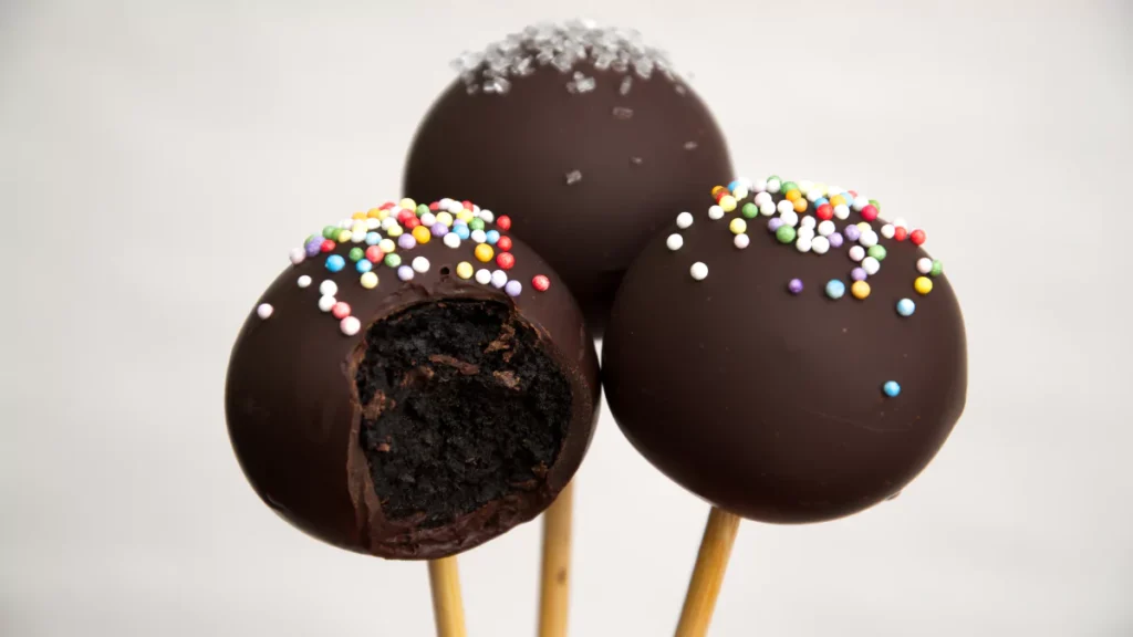 A tray of vibrant Starbucks-style cake pops with colorful coatings, sprinkles, and elegant drizzle designs on a stylish dessert table.