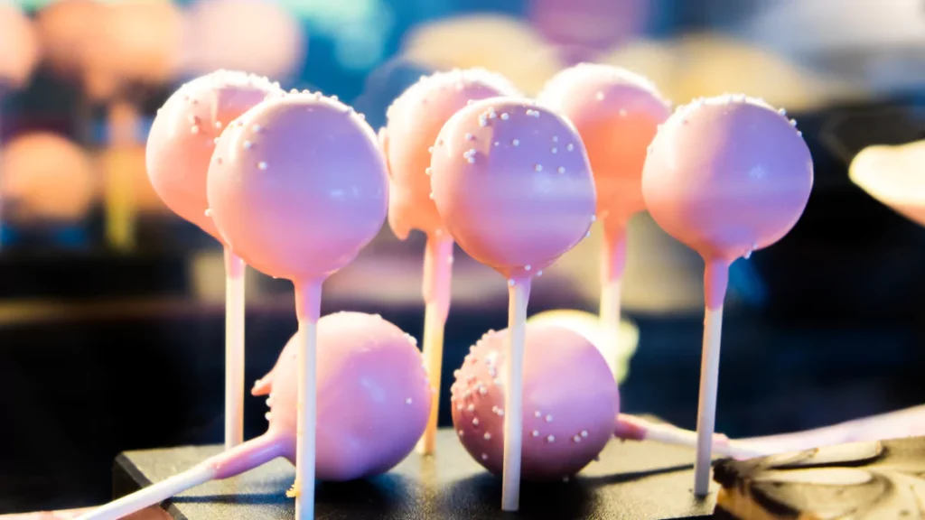 Close-up of a Starbucks cake pop with vibrant pink candy coating and white sprinkles.