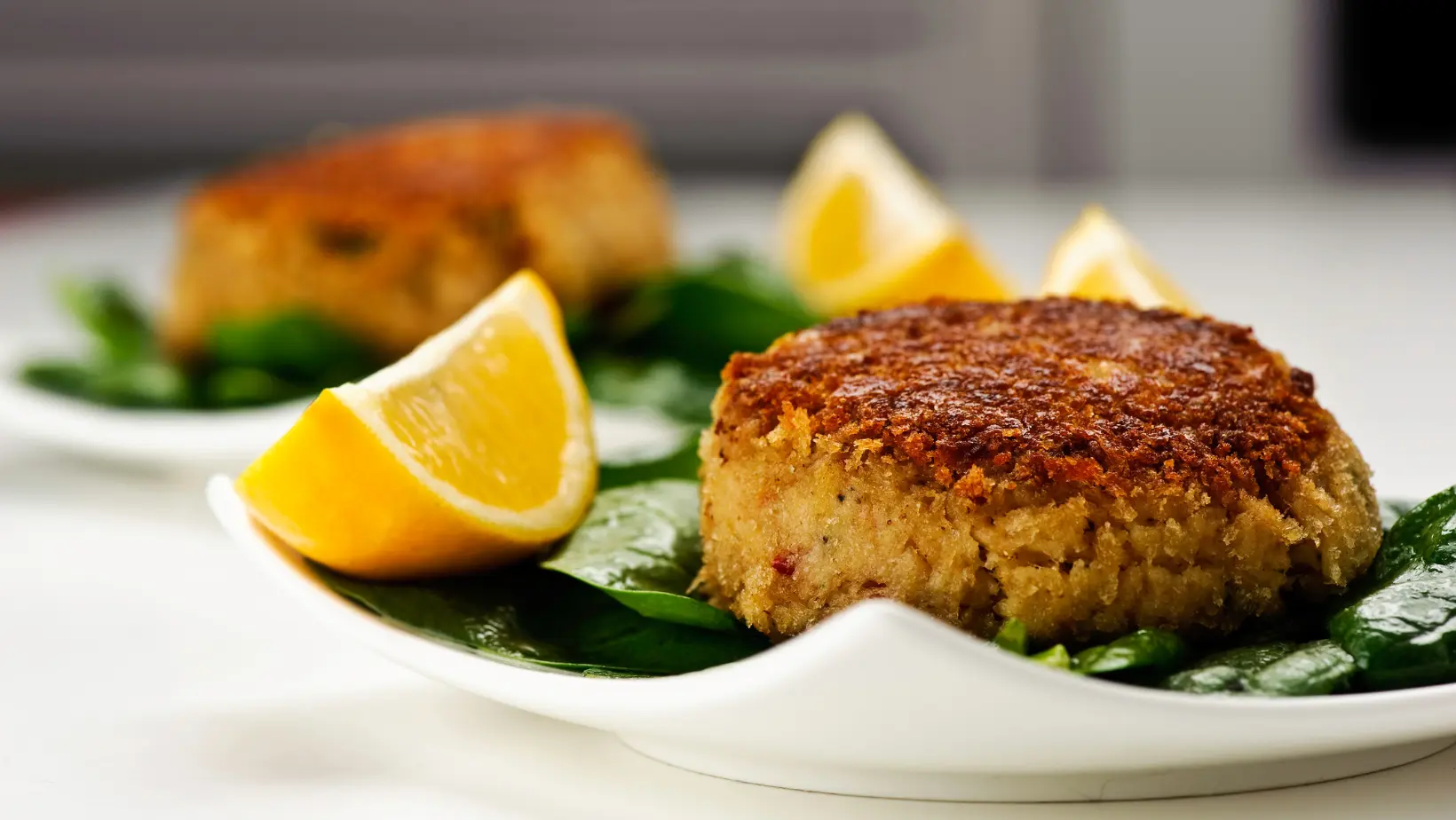 Firm crab cakes on a plate with lemon slices and dipping sauce.