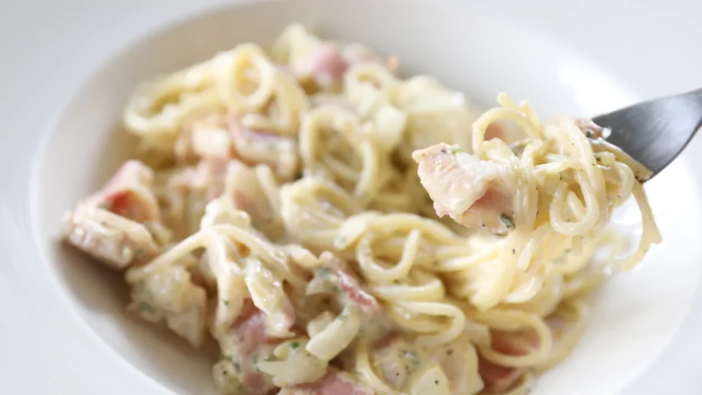 Silken tofu pasta with creamy Alfredo sauce, garnished with parsley and served in a white bowl.