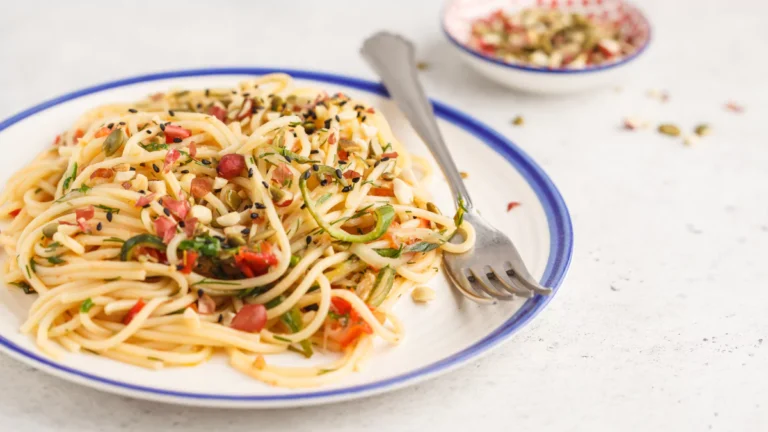 A plate of vegan pasta with creamy silken tofu sauce, garnished with parsley and surrounded by fresh ingredients like basil, garlic, and cherry tomatoes.